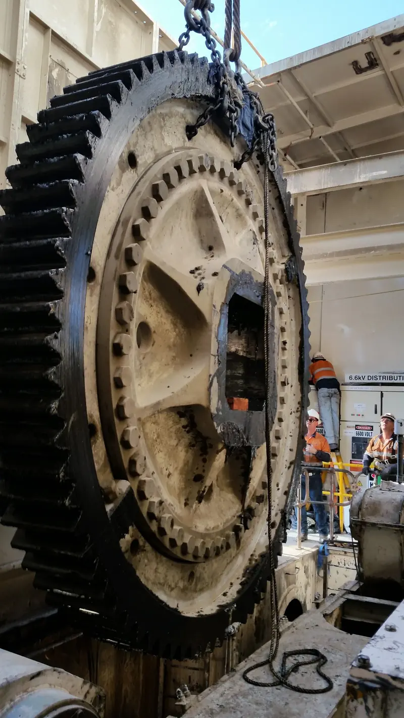 Large drive gear lifted out of a dragline machinery house with crew watching