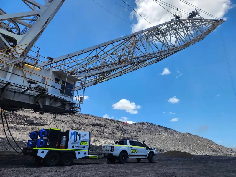 Marquee service trailer and ute parked under a dragline boom in an open-cut coal mine